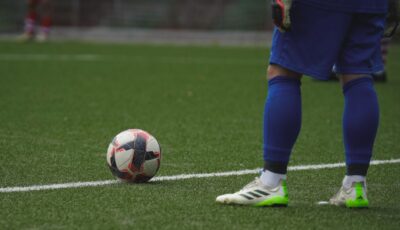 Close-up of a football player standing by a ball during a game on a grass pitch.