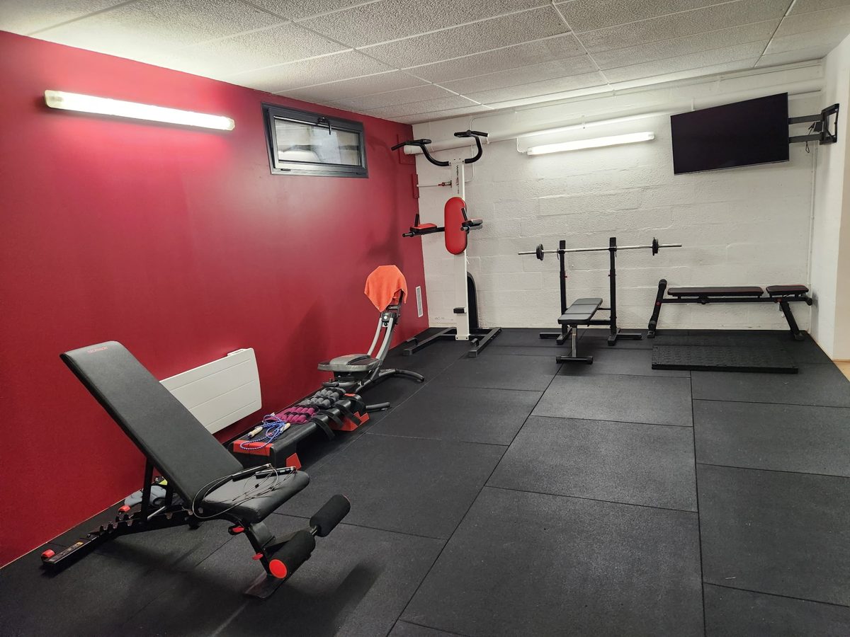 Home gym aménagé avec un sol en dalles de caoutchouc noires, banc de musculation et rack